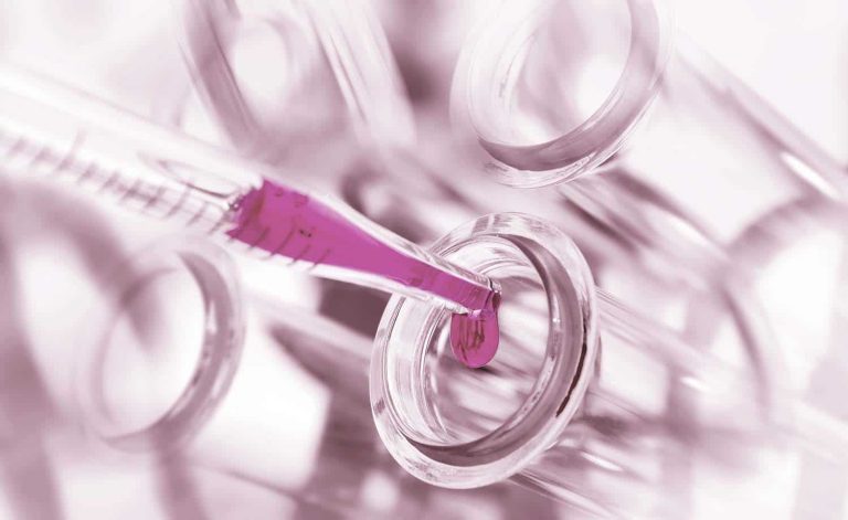 Nahaufnahme einer Laborpipette mit pinkfarbener Flüssigkeit, die in ein Reagenzglas getropft wird – Symbol für Forschung und Qualitätskontrolle