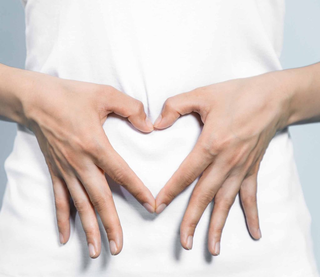 Hände formen ein Herz über dem Bauch – Symbol für Darmgesundheit und Wohlbefinden
