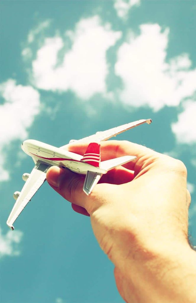Hand hält ein Modellflugzeug gegen den Himmel – Symbol für unbeschwertes Reisen