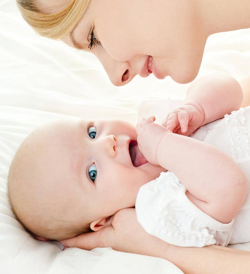 Mutter hält ihr Baby liebevoll im Arm, beide liegen auf einem weißen Bett und schauen sich zärtlich an