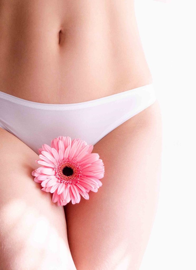 Symbolische Darstellung weiblicher Intimgesundheit: Unterleib einer Frau in weißer Unterwäsche mit rosa Blume als Sinnbild für eine gesunde Scheidenflora